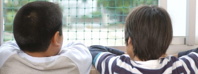 校舎内から外を見る小学生の背中